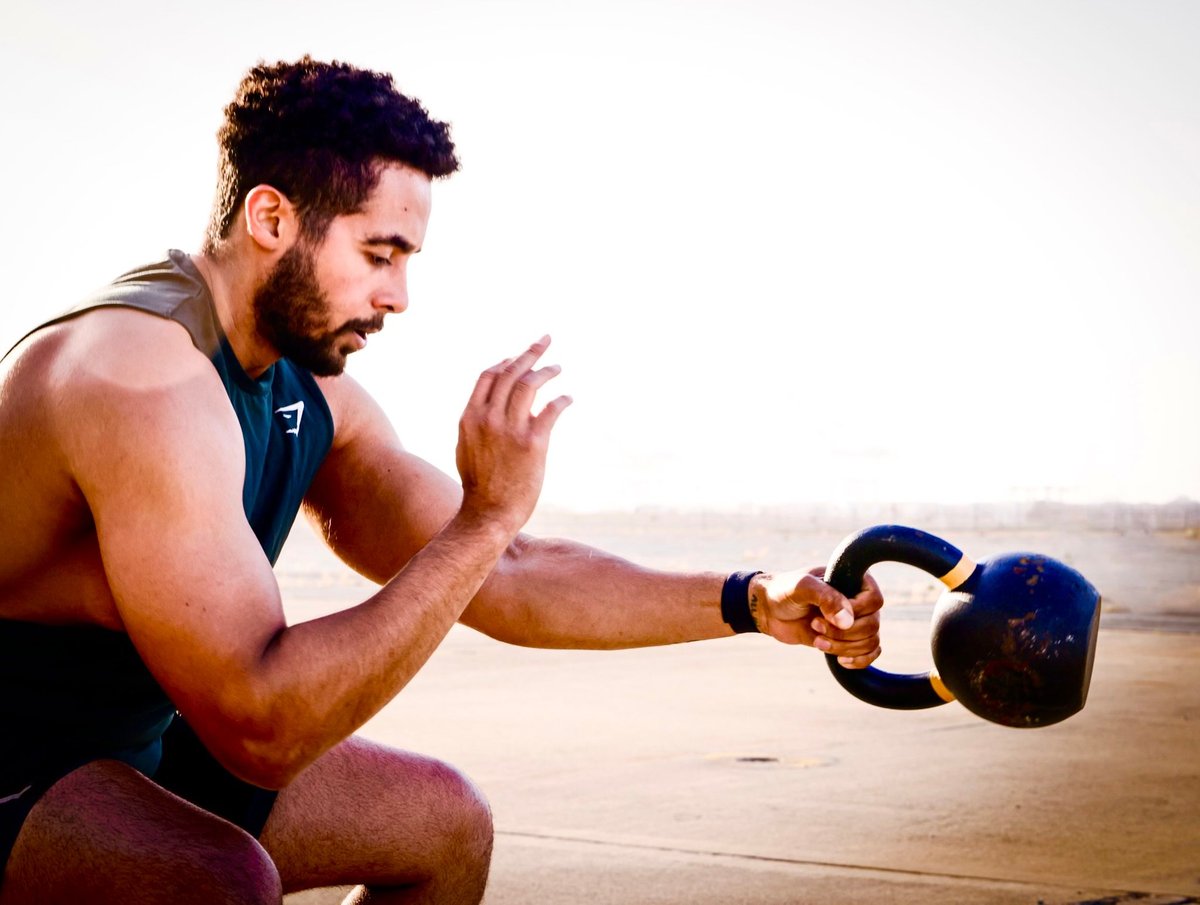 Man performing kettlebell exercise in squat position on wooden floor with outdoor background